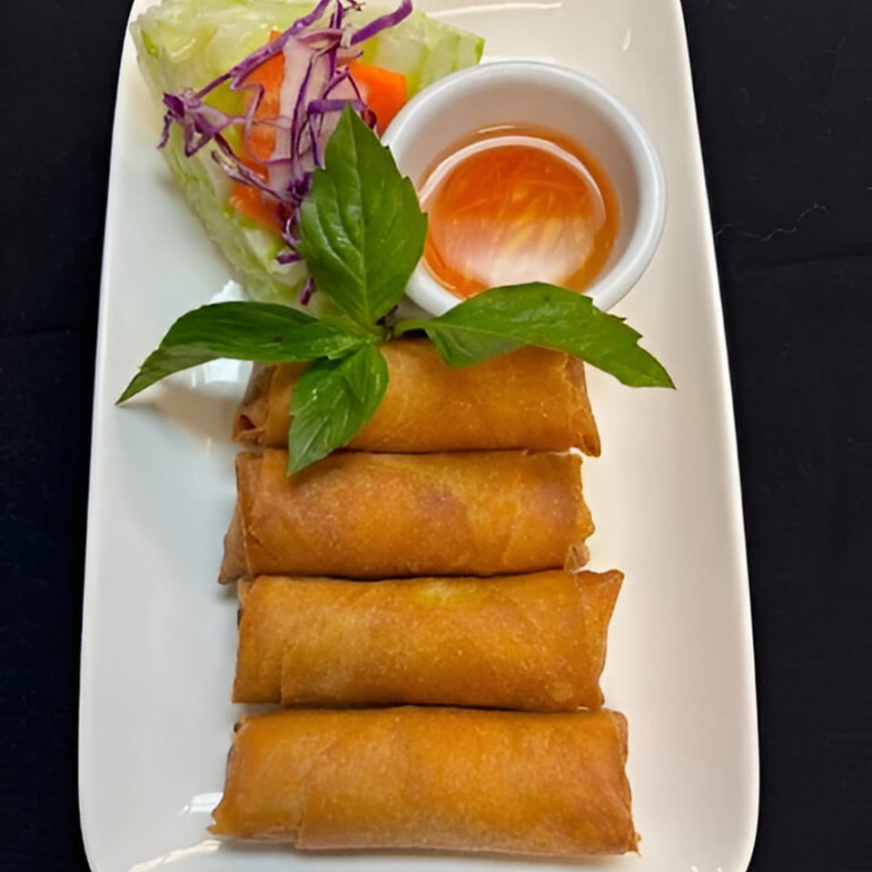 Four golden-brown Vietnamese spring rolls with a side of sweet chili sauce and fresh salad.