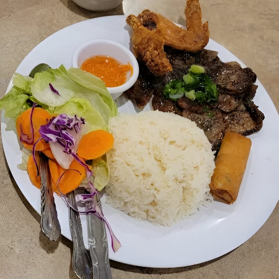 Vietnamese grilled pork, fried chicken wing, spring roll, rice, and fresh salad on a white plate.
